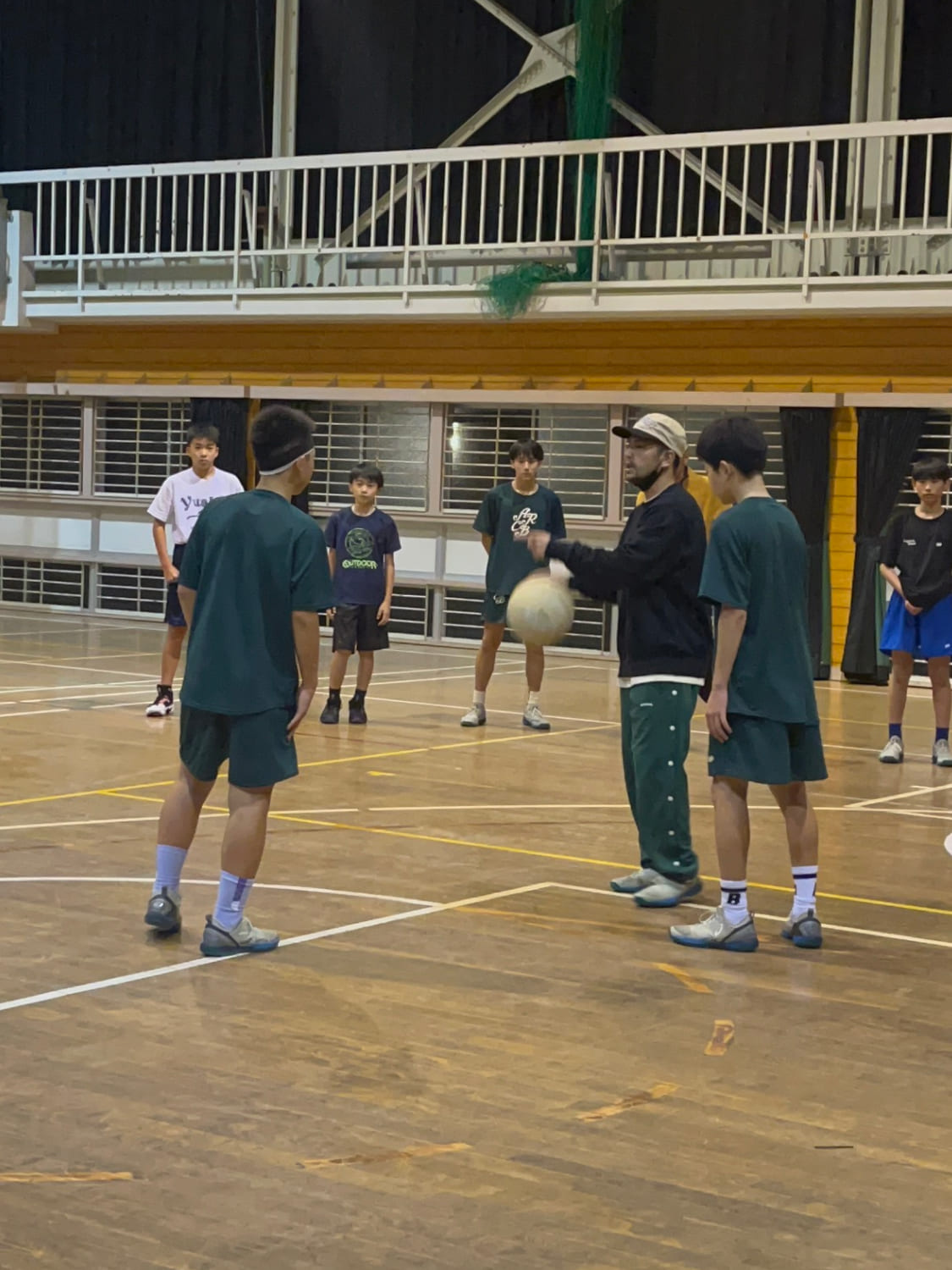 コーチがスクール生にバスケットボールを教えている様子の写真