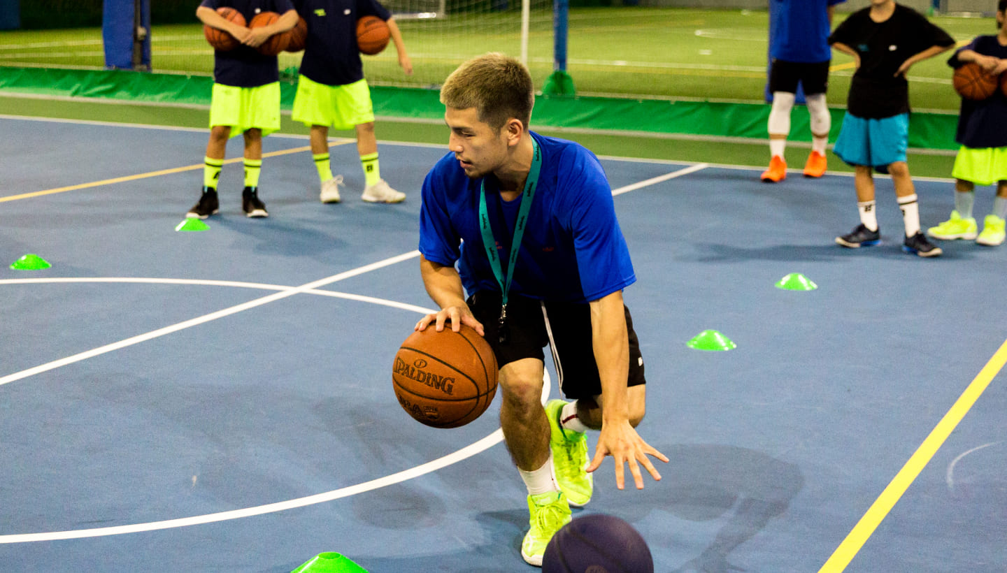 コーチがドリブルをしながら、子供達にバスケットボールを教えている様子の写真