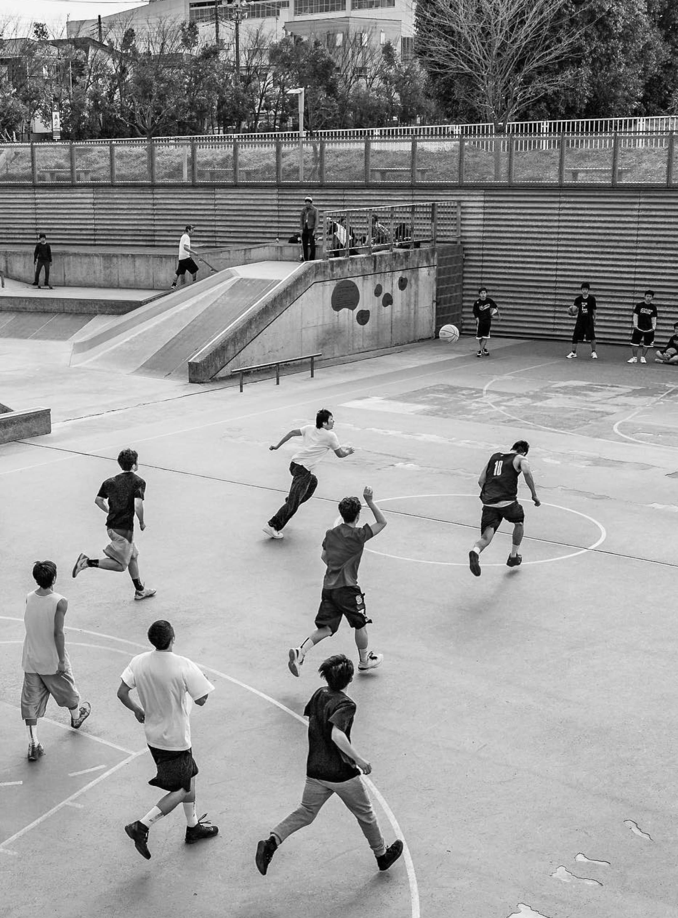 複数人の大人が野外でバスケットボールを楽しんでいる様子の白黒写真