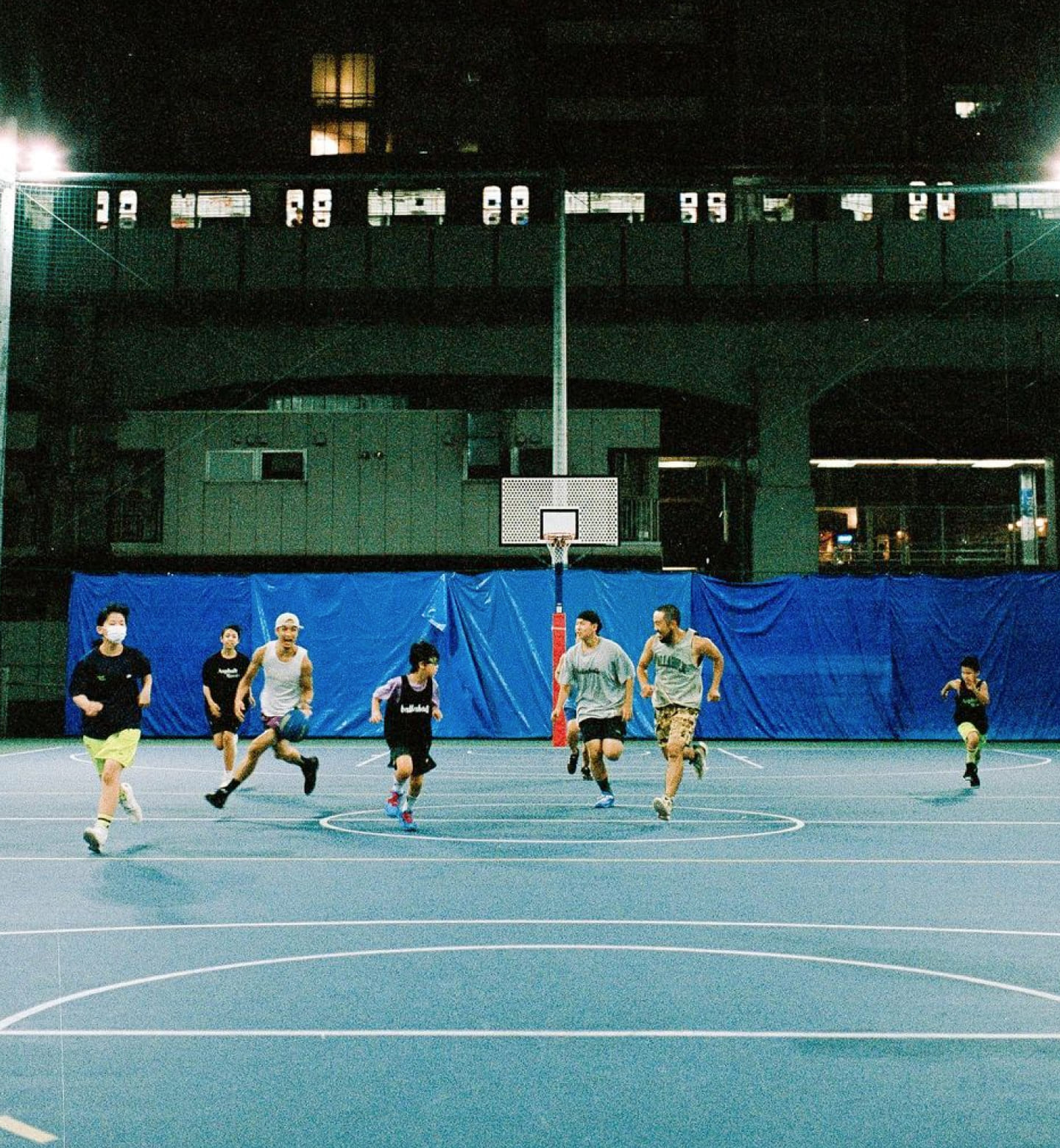 大人と子供が混ざって、一緒にバスケットボールの試合をして楽しんでいる様子の写真