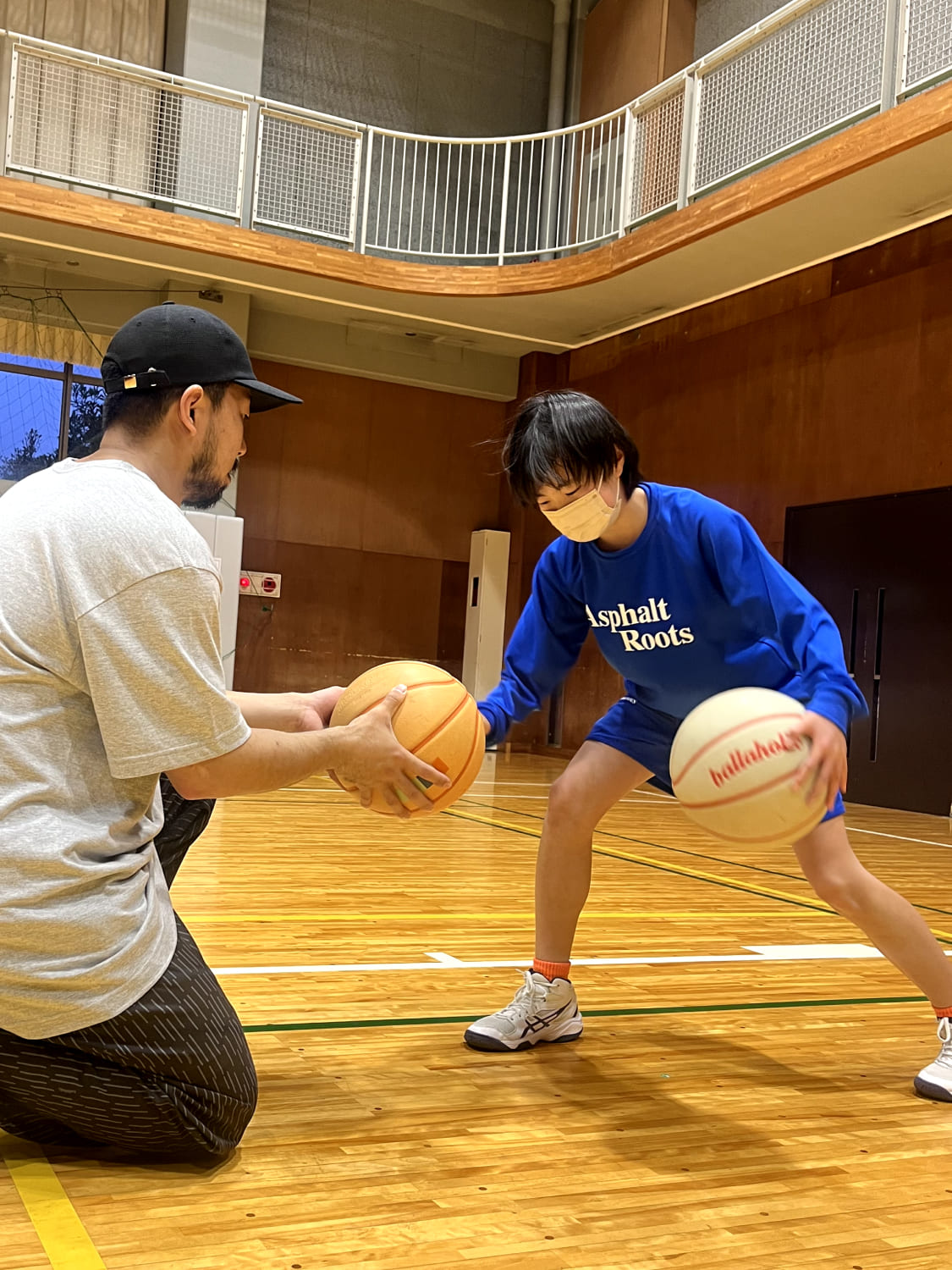 スクール生がコーチにバスケットボールを教えてもらっている様子の写真