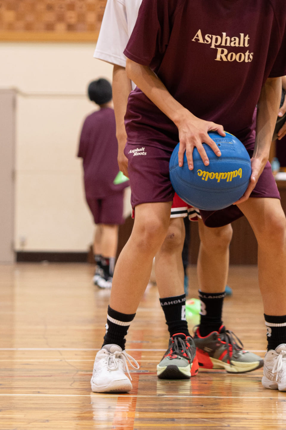 えんじ色のTシャツを着た人がバスケットボールを両手で持っている様子の写真