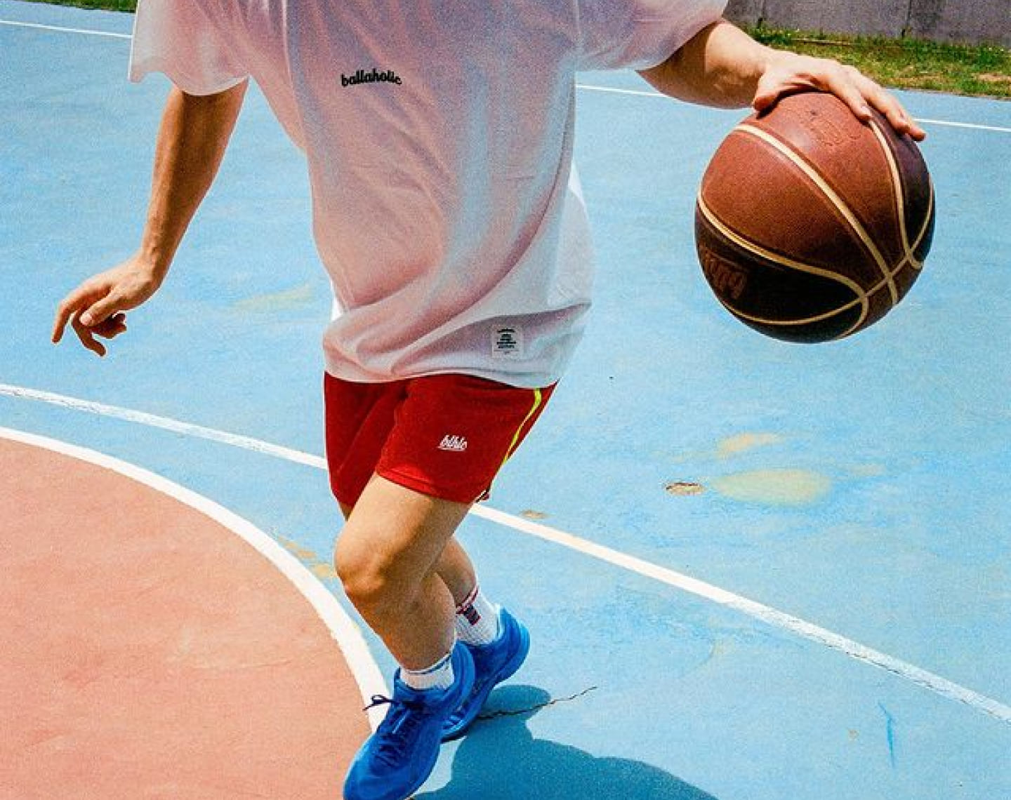 白いTシャツ、赤いパンツ、青いシューズを履いた青年がバスケットコートでドリブルをしている写真